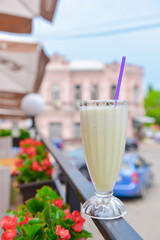 Vanilla milkshake in a tall glass with a plastic straw outside. Delicious dessert drink, refreshing summer beverage.