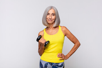 middle age woman smiling happily with a hand on hip and confident, positive, proud and friendly attitude. fitness concept