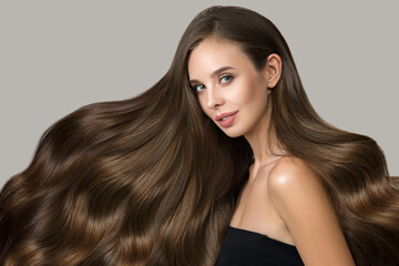 Portrait of a beautiful young brunette with wavy hair. Woman with hairstyle and makeup on gray background