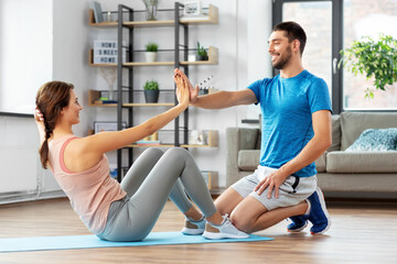 Wall Mural - fitness, sport, training and healthy lifestyle concept - woman with personal trainer doing sit ups at home