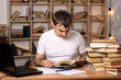 © Олег Кононов - young male student sits at a table with books on the background of a cabinet. office worker examines documents. European look. distance learning. preparation for exams.