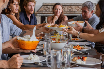 Diverse group of multiethnic friends enjoying meal sharing and passing food to each other in outdoor cafe or home. Leisure, food and drinks, people and holidays concept