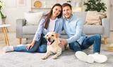 Fototapeta Zwierzęta - Young happy spouses with dog sitting in living room