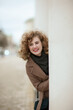 © Kiryakova Anna - A portrait of a curly-haired young woman peeking out from behind a white pillar. Smiling girl looking at camera
