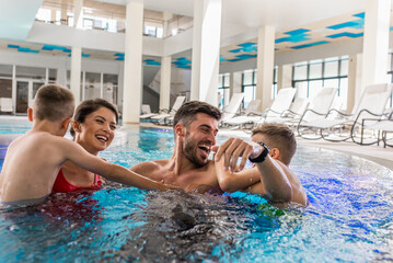 Wall Mural - smiling family of four having fun and relaxing in indoor swimming pool at hotel resort.