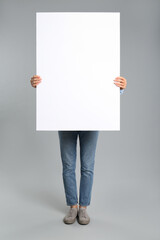 Sticker - Woman holding white blank poster on grey background. Mockup for design