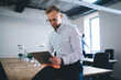 © BullRun - Serious caucasian businessman in eyewear for vision correction checking mail on digital tablet during working process in office, confident male millennial freelancer reading news online on touchpad