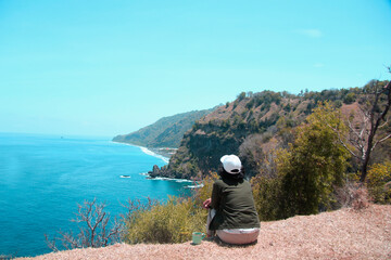 Wall Mural - Person watching the sea. Young woman sitting alone  looking at the blue beach view, relax with a coffee cup.