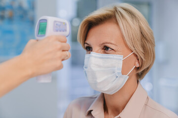 Receptionist checking fever middle age woman by digital thermometer for fever scan. Healthcare concept