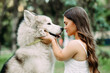 Young dwarf woman embraces Malamute dog in park.