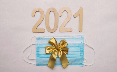 Light wooden numbers 2021 lie on a white background with a gold bow and two medical disposable masks