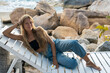 © mizuno555 - Portrait of a smiling happy young caucasian woman in jeans with long blond hair lies on a white wooden beach lounger by the sea with a frangipani flower in her hand