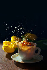 A cup of black tea flowing in cup against yellow flowers and black background