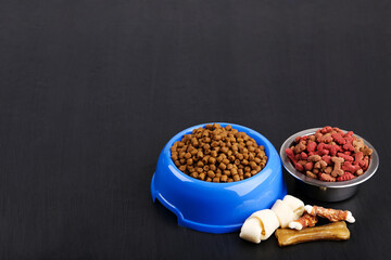 Wall Mural - Dry pet food in bowls with bones on black background