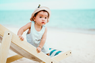 9 Months  asian baby sitting on beach chair with sea beach as background, summer concept