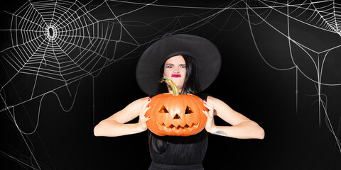 Wall Mural - Young woman in black hat on scary black background. Attractive caucasian female model. Halloween, black friday, cyber monday, sales, autumn concept. Flyer for your ad with copyspace. Holding pumpkin.