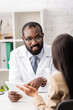 © LIGHTFIELD STUDIOS - african american doctor in eyeglasses pointing with finger at digital tablet during conversation with patient