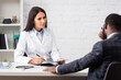 © LIGHTFIELD STUDIOS - selective focus of african american patient touching face while sitting opposite brunette doctor