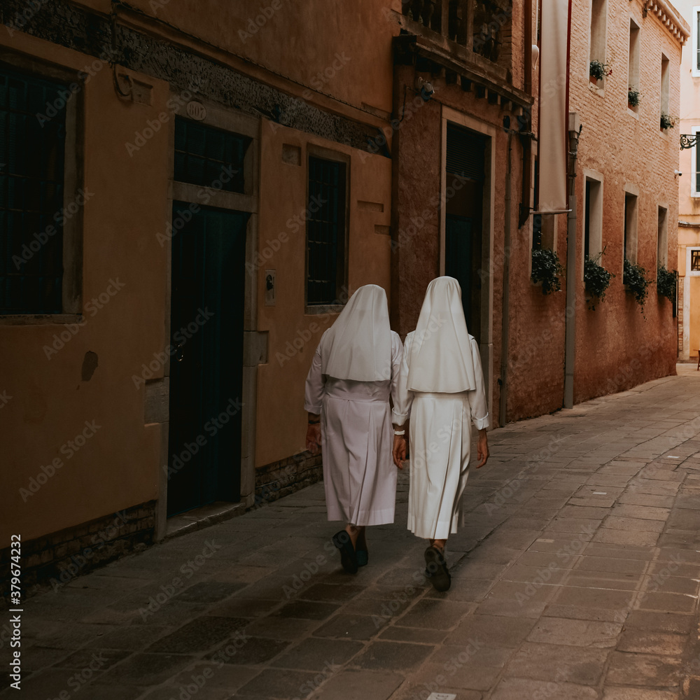 Two nuns in white robes are walking along the narrow streets of the ...