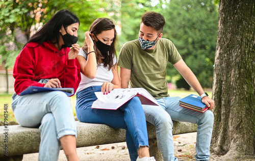 Fotomural Three students studying together sitting on a bench outdoor and wearing masks du