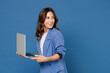 © ViDi Studio - Smiling cheerful beautiful attractive young brunette woman 20s wearing basic jacket standing working on laptop pc computer looking aside isolated on bright blue colour wall background studio portrait.