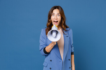 Excited surprised amazed cheerful funny beautiful young brunette woman 20s wearing basic jacket screaming in megaphone looking camera isolated on bright blue colour wall background studio portrait.