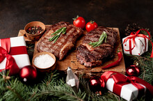 Christmas Dinner For Two, Grilled Beef Steak Ribeye, Herbs And Spices On A Stone Table With A Christmas Tree And New Year's Toys	