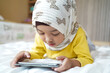 © Asada - Asian Muslim kid playing smartphone at home.