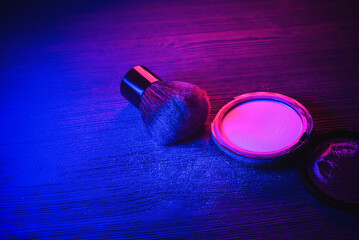 Face powder and make up brush on the table in the neon lights background.