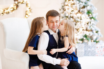 Wall Mural - father and daughter on a chair on the background of a Christmas tree. happy fatherhood. new year vacations.