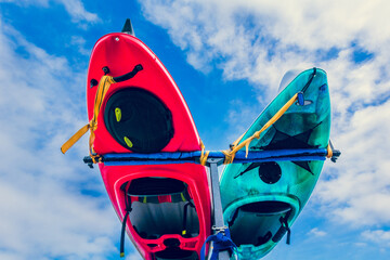 Underside of kayaks tied to rack on back of vehicle against blue sky with clouds