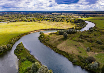 Wall Mural - a panoramic view of the white old church on a green meadow between the tributaries of the river against the backdrop of thunderclouds filmed from a drone