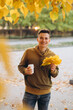 © anatoliycherkas - Handsome and happy guy with a bouquet of yellow leaves smiling and drinking coffee in autumn park