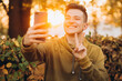 © anatoliycherkas - Portrait of handsome and happy guy smiling and holding a bouquet of autumn leaves and taking a selfie in the park