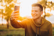 © anatoliycherkas - Portrait of handsome and happy guy smiling and holding a bouquet of autumn leaves and taking a selfie in the park
