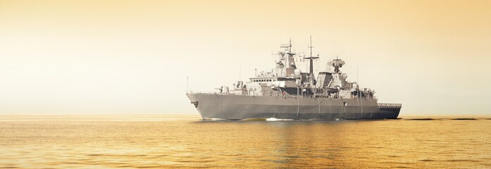 Canvas Print - Large grey modern warship sailing in still water. Clear sky. Golden sunset light. Baltic sea, Germany. Global communications, international security theme. Panoramic image