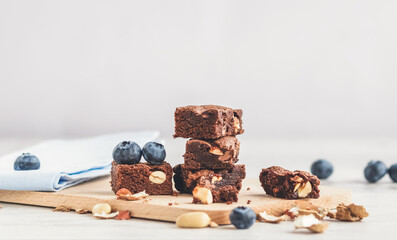 Selective focus to pieces of chocolate brownie with peanuts on a wooden board in a soft light. Copy space.