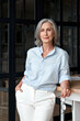 © insta_photos - Confident stylish mature middle aged woman standing at workplace. Stylish older senior businesswoman, 60s grey-haired lady executive leader entrepreneur looking at camera in office, vertical portrait.