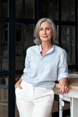 Wall Mural - confident stylish mature middle aged woman standing at workplace. stylish older senior businesswoman