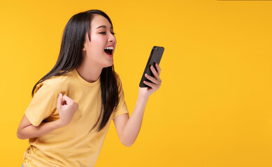 Cheerful young woman holding smartphone with shocked amazed for success or get good news over isolated yellow background.