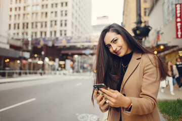 Wall Mural - Beautiful girl in a city. Stylish brunette in a brown coat. Woman in a Chicago. Lady with a phone