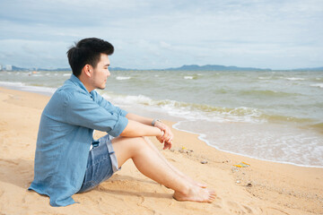 Lonely asian man sitting alone looking at the sea on the beach.