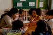 © twinsterphoto - Young woman working in school helping children with arithmetic, learning about mathematics, counting. Asian school teacher assisting multiethnic students in classroom