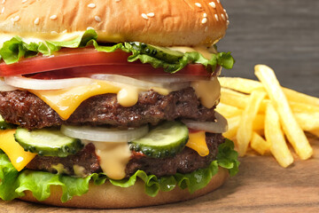 Huge tasty beef hamburger with french fries close-up. Juicy cheeseburger or burger with two bbq meat patties or cutlet, lettuce, salad, tomato, onion, pickles and sauce. American classic fast food.