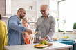 © DC Studio - Man pouring wine to his father in kitchen during family lunch.