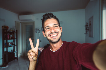 happy young handsome millennial taking a selfie smiling at the camera in the living room at home.