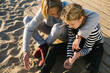 © BONNINSTUDIO/Stocksy - Overhead of grandmother and her granddaughter sitting together on the beach in autumn.
