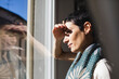 © Michela Ravasio/Stocksy - Brunette woman looks out the window