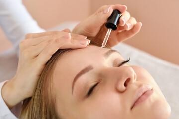 Wall Mural - Closeup of beautiful woman receiving serum for skin moisturizing from pipette. Beauty, skincare cosmetology.