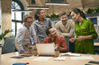 © Friends Stock - Group of young happy multicultural business people looking at laptop screen and discussing work or project results while standing in the modern office or coworking space